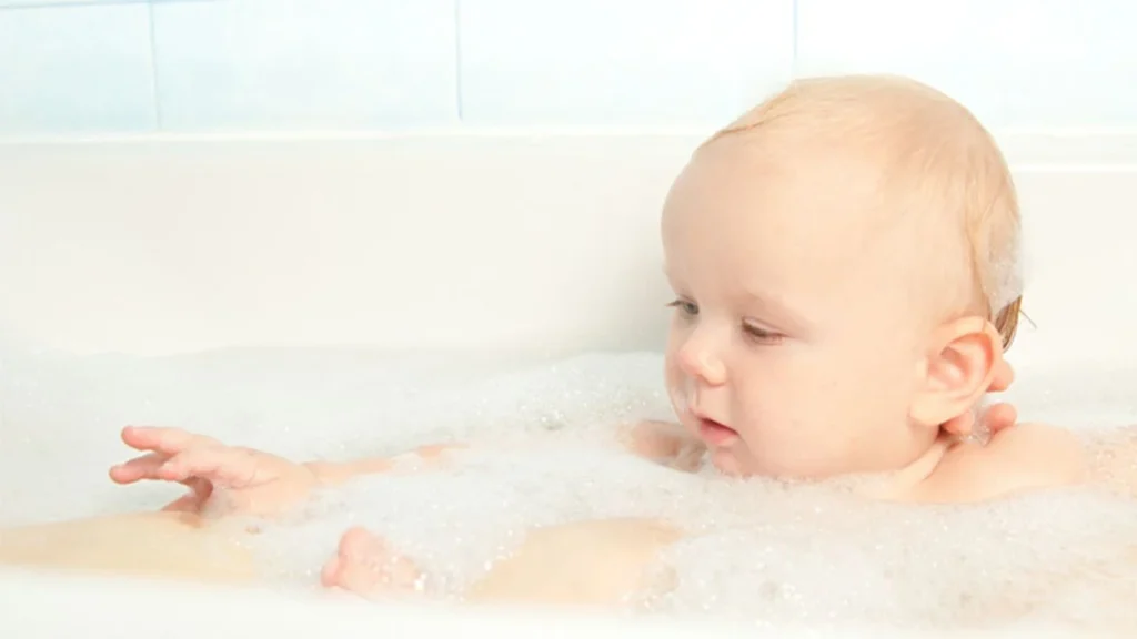 Baby sitting in a bathtub filled with bubbles, giggling uncontrollably.
