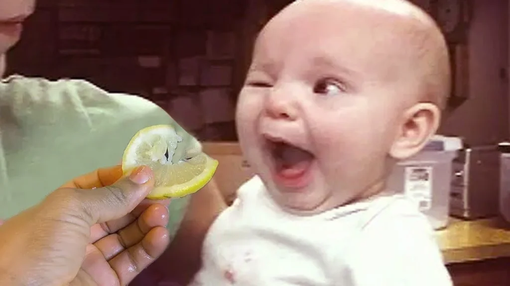 Baby attempting to eat a lemon slice and making a hilarious sour face, followed by a cute smile.