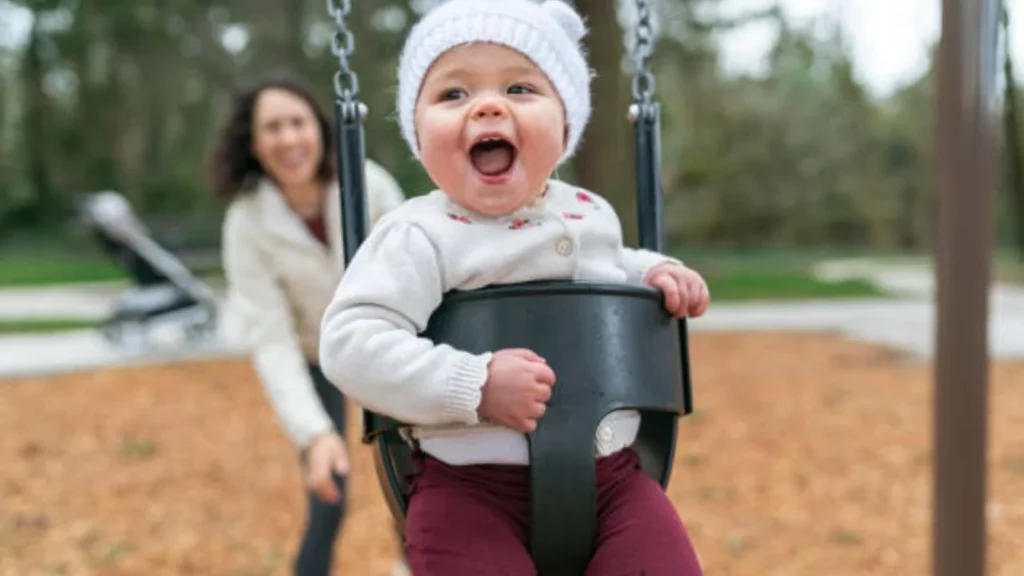 Baby sitting in a swing and laughing as they go back and forth.
