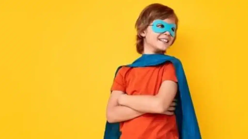 Baby wearing a superhero cape and striking a pose with a proud smile.